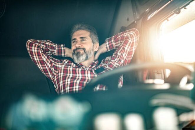 Happy truck driver wearing casual clothing sitting in his truck, chilling and smiling.