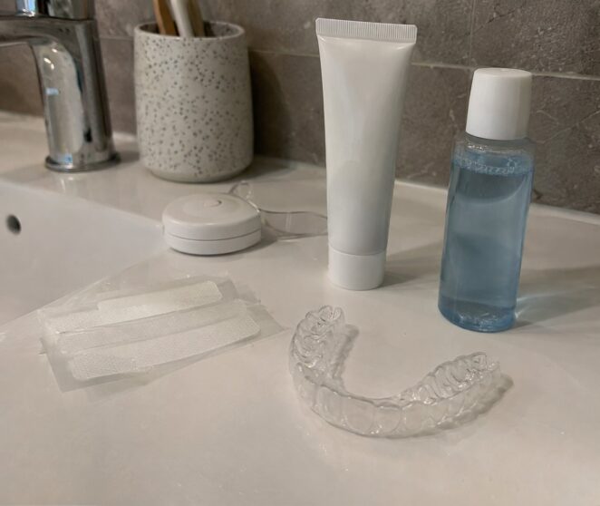 Whitening strips, dental tray, toothpaste, and mouthwash on a bathroom counter.