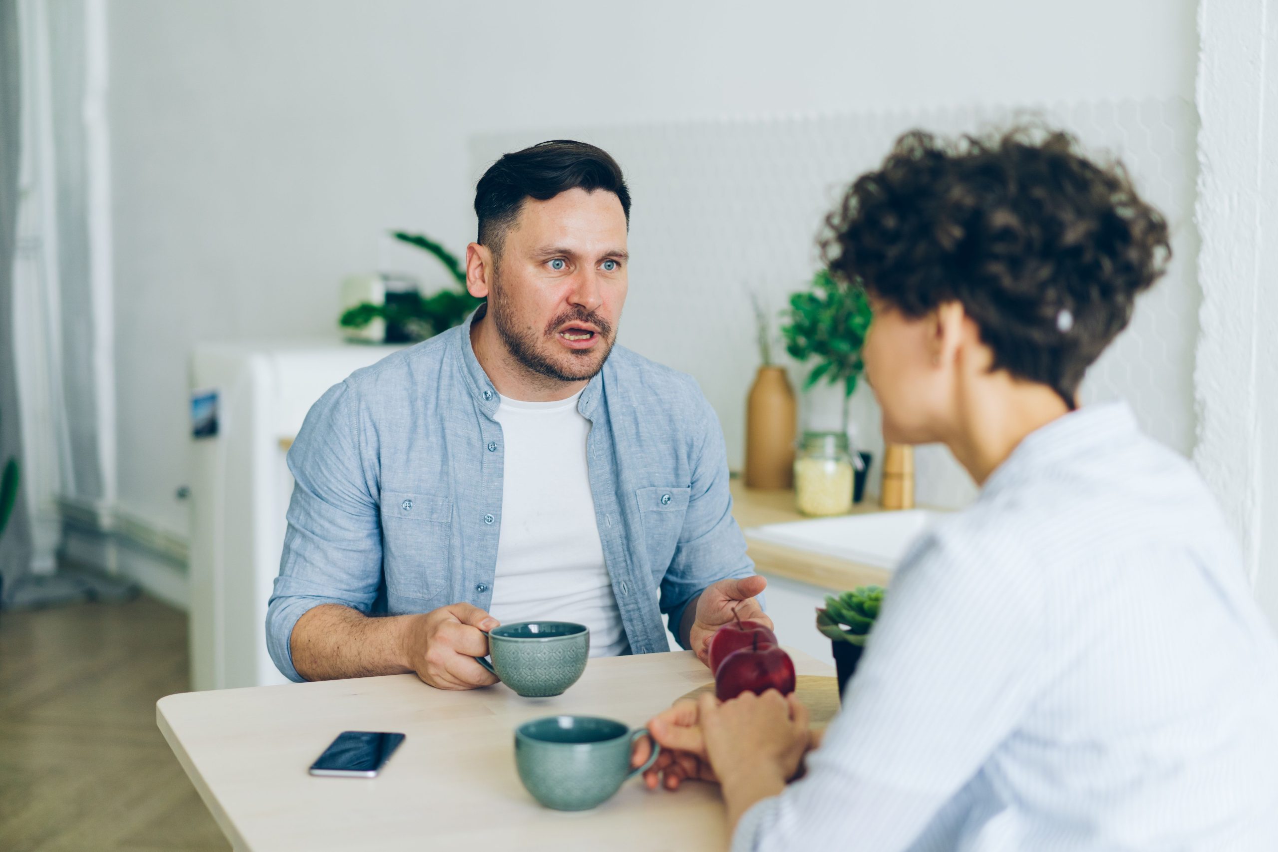 Couple having a serious, open conversation at the kitchen table over coffee cups