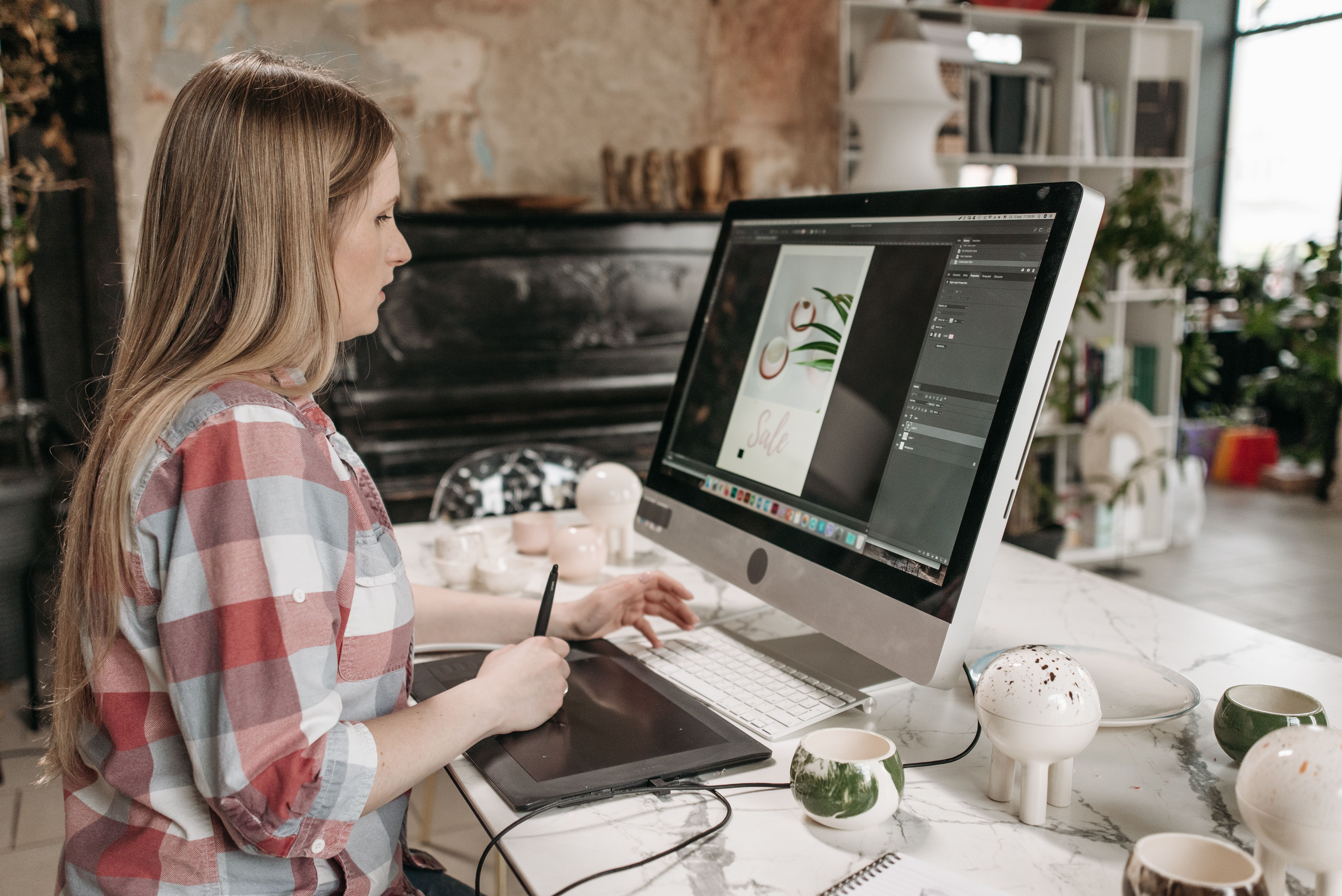 Woman using a digital drawing tablet in a workspace, editing social media graphics without hiring a designer